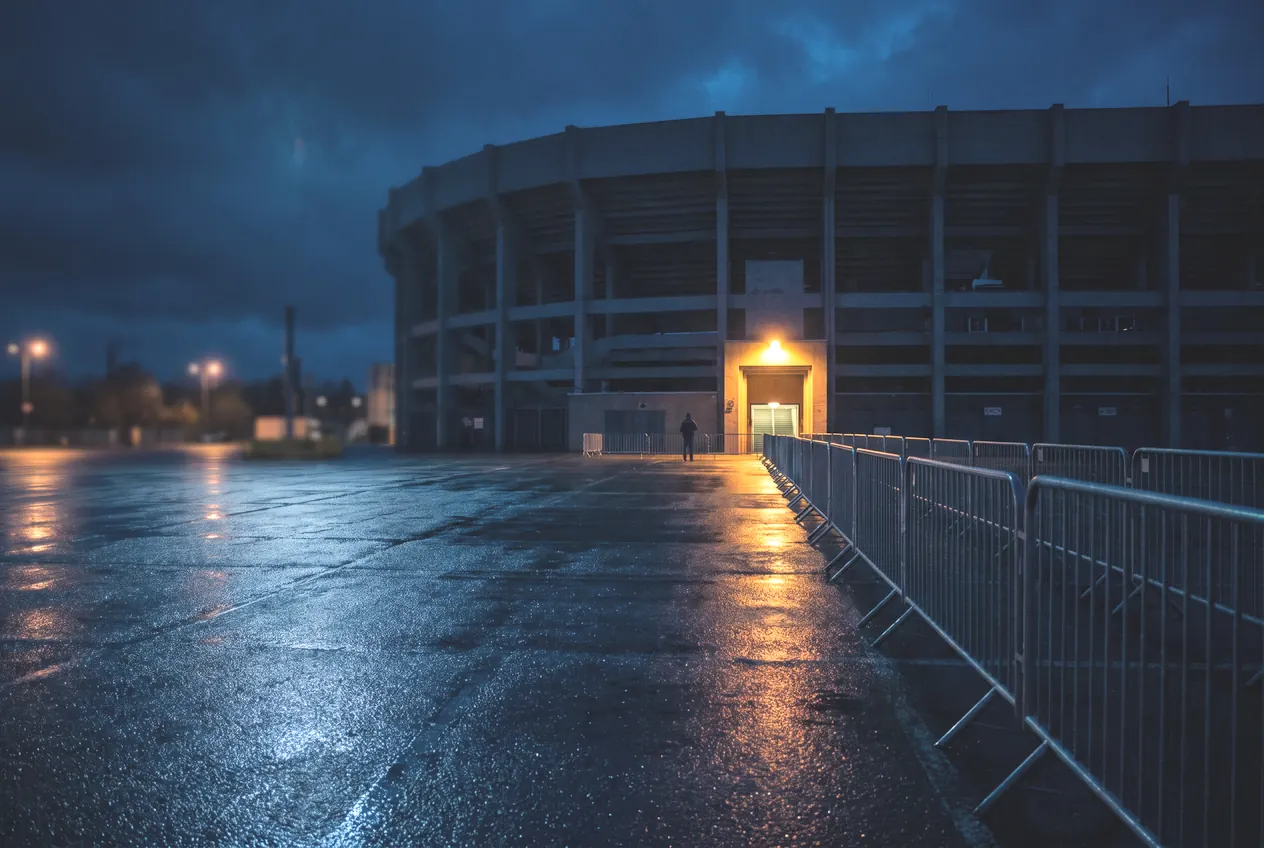 A single lit entrance on the side of a stadium across an empty wet forecourt