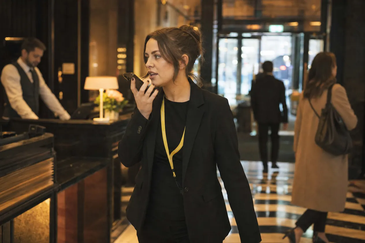 A duty manager speaking into a phone as she crosses the lobby of a bar