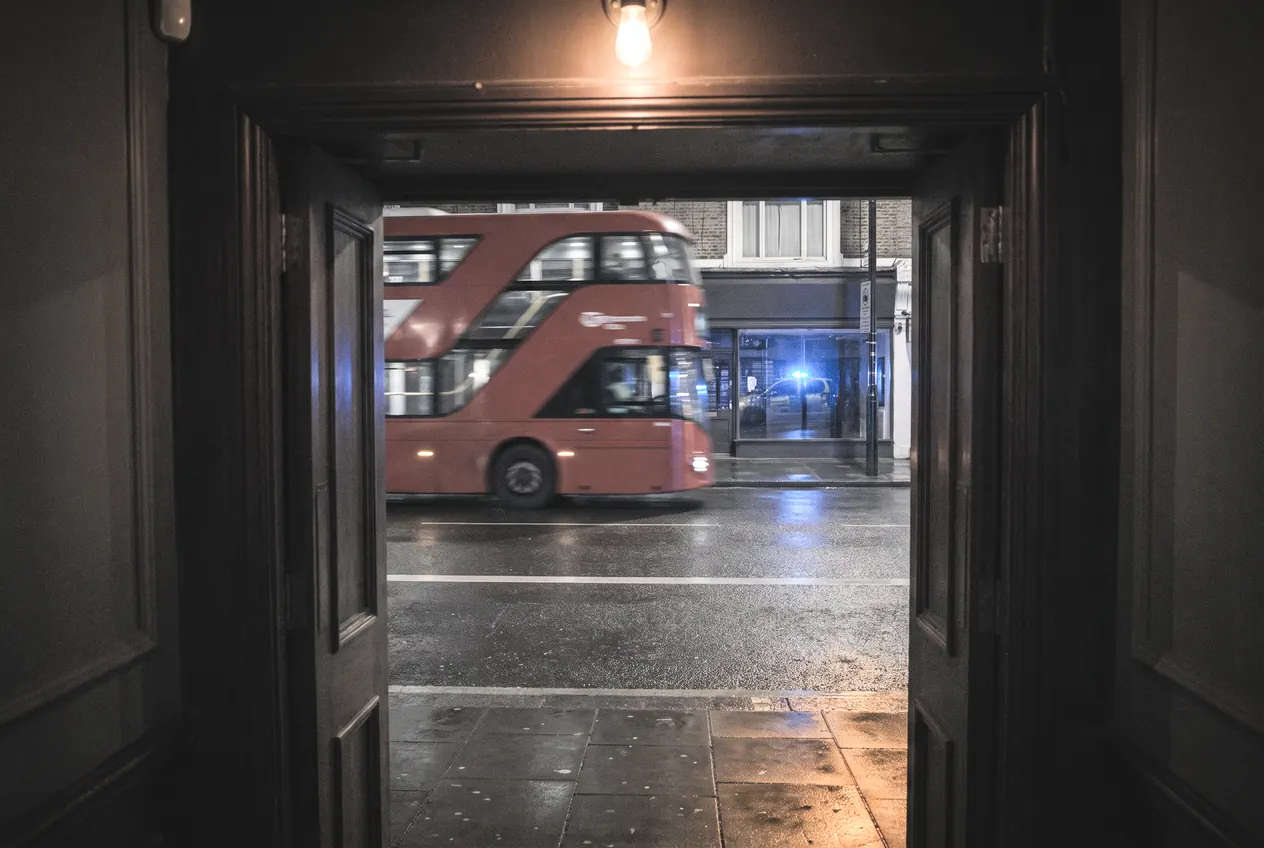 A London bus and blue lights passing the open doorway of a bar at night