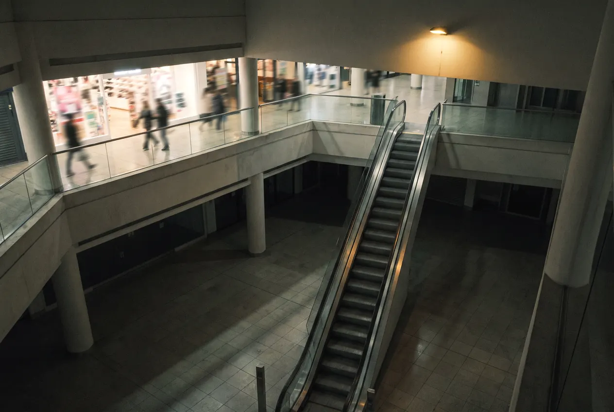 Escalators between two floors of a shopping centre, shoppers moving on the level above