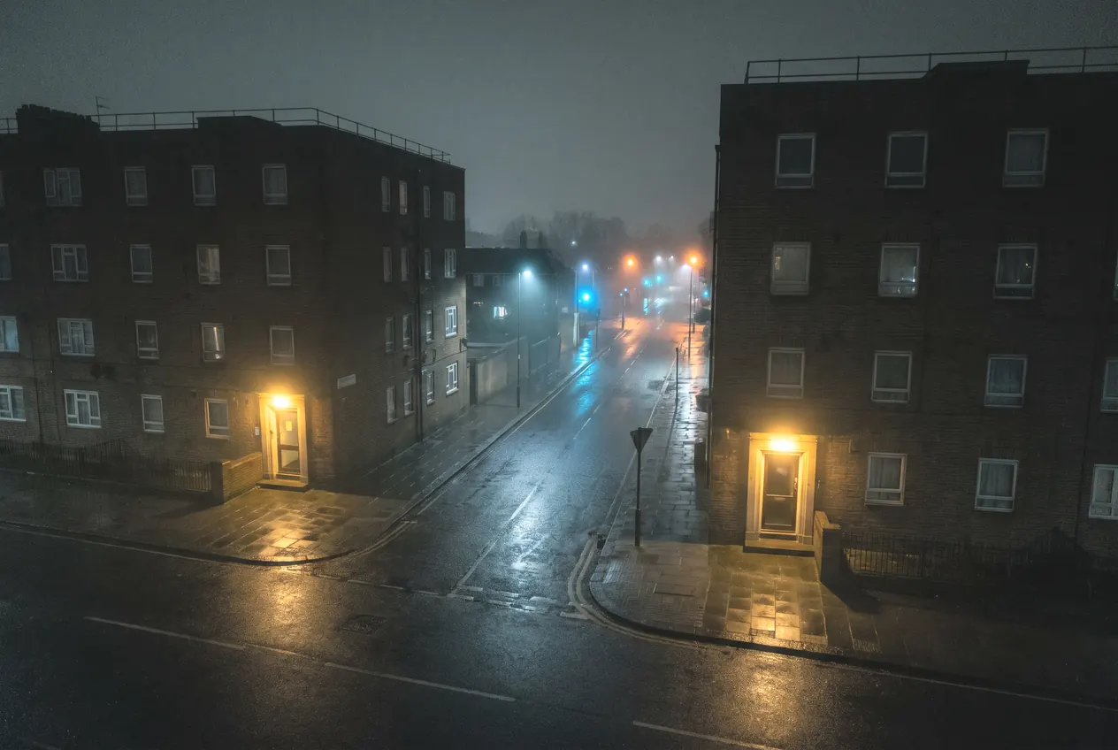 A misty street running between two residential blocks, seen from above at night