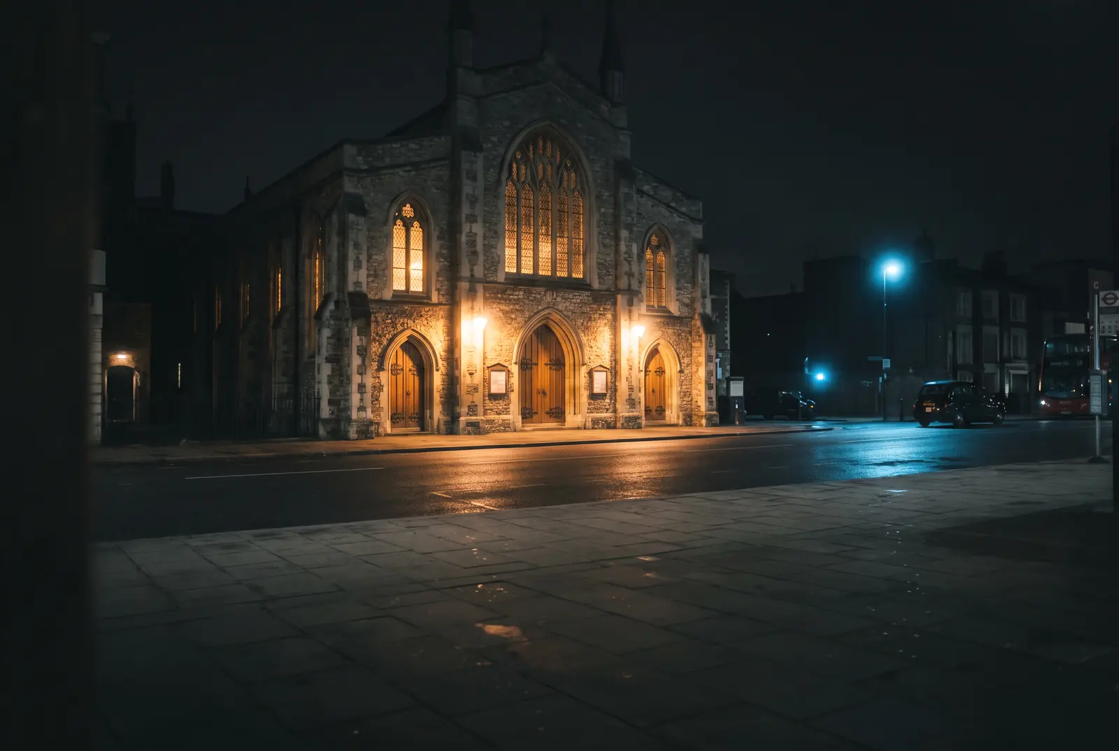 A church on a city corner at night, its doors and windows lit above the empty pavement