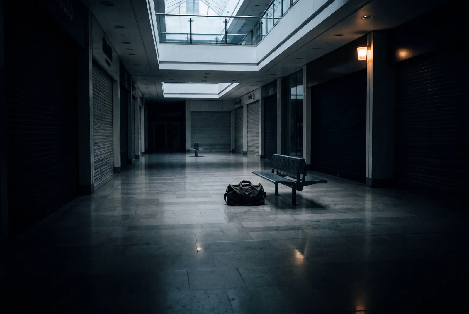 An unattended holdall beside a bench in a closed shopping centre mall, shutters down