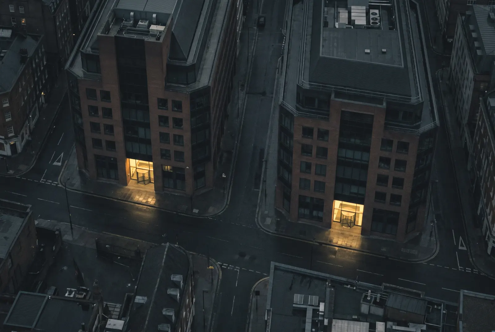 Two office blocks seen from above at night, each with a single lit reception at street level